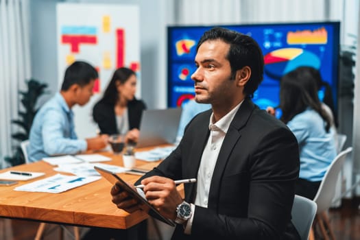 Portrait of businessman or analyst looking at camera with his colleague analyzing data analysis in dynamic business strategy investment planning meeting. Meticulous