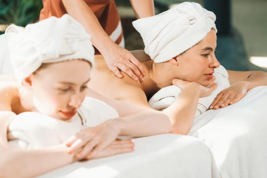 A couple of beautiful young woman with white towel lie on comfortable spa bed during receive relaxing body massage by professional masseur surrounded at spa salon. Gray background. Tranquility.