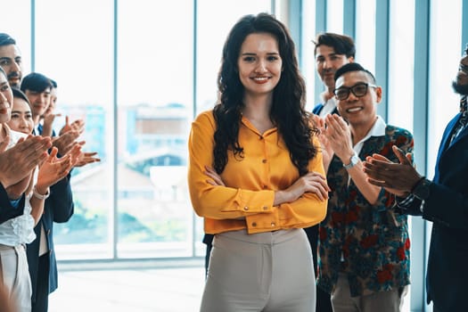 Successful businesswoman looking at camera with confidence while standing rounded with her coworker clapping hands. Diverse team celebrates promotion of new beautiful manager. Intellectual.