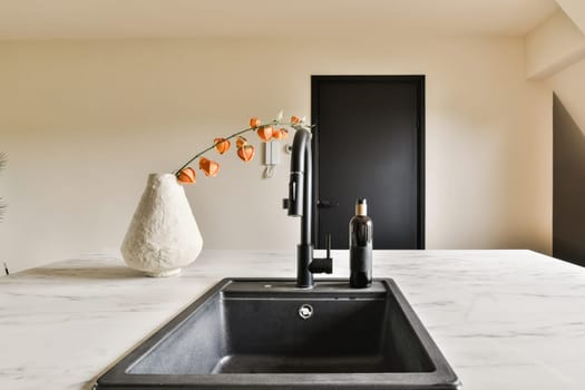a kitchen with marble countertops and black faucets in the sink is next to a white vase that has an orange flower