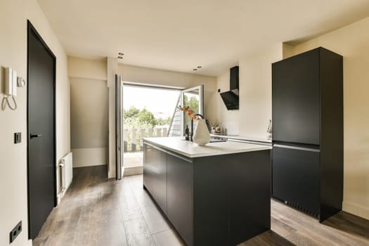 a kitchen with wood flooring and black cabinetd cupboards on the wall behind it is a large open door that leads to an outdoor patio