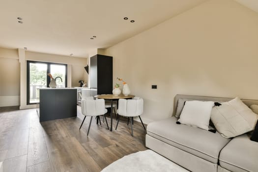 a living room with wood flooring and white couches in the center of the room is an open kitchen area