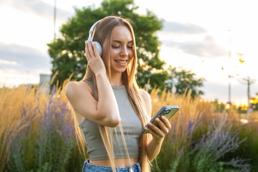 Portrait of young blonde listening to music with headphones and smiling selective composition in the park