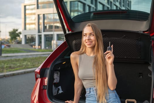 Happy blonde woman buying new red car, raising hand up with automatic key