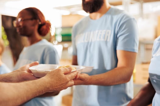 Close-up of a male charity worker handing out free food to the poor and homeless people. Volunteer holding a meal box to give to the hungry and less fortunate at an outdoor food bank.