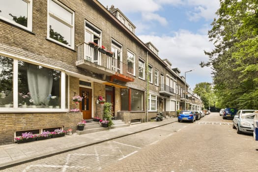 a city street with cars parked on the side and buildings in the back ground, some flowers are hanging from windows