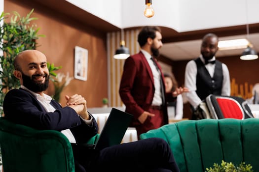 Businessman preparing for conference in hotel lobby, working on laptop after arriving at resort. White collar worker in formalwear waiting to register for room, travelling for work.