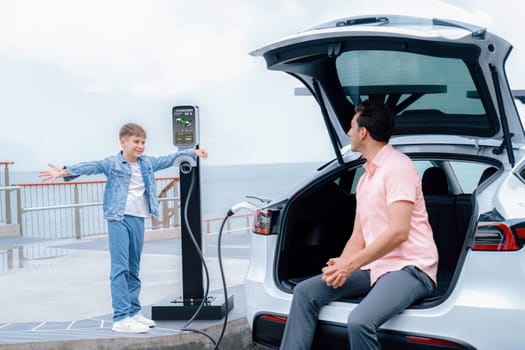 Family road trip vacation traveling by the sea with electric car, father and son recharge EV car with green and clean energy. Natural travel and eco-friendly car for sustainable environment. Perpetual