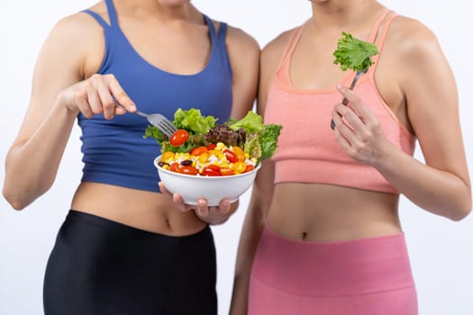 Two young sporty Asian women in sportswear holding salad bowl fill with fruit and vegetable. Natural youthful and fit body lifestyle people with balance nutrition on isolated background. Vigorous