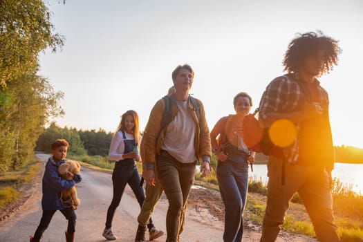 A group of friends, boys and girls, tourists with a little boy walk along the shore of the lake against the backdrop of the setting sun at Golden Hour, high quality photo