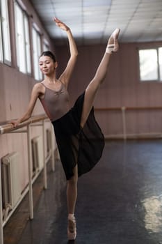 Graceful Asian ballerina in a beige bodysuit and black skirt is rehearsing in a dance class