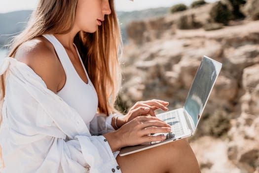 Digital nomad, Business woman working on laptop by the sea. Pretty lady typing on computer by the sea at sunset, makes a business transaction online from a distance. Freelance remote work on vacation