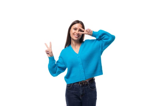 young positive pretty caucasian woman with black hair is dressed in a stylish blue cardigan and jeans on a white background.