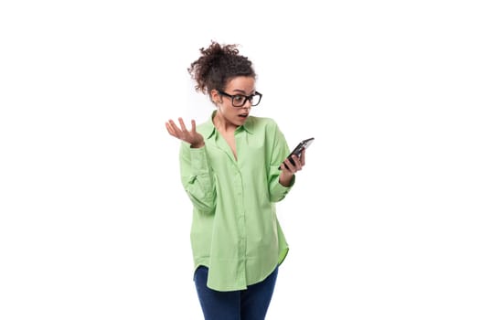 a young brunette businesswoman with curly hair is dressed in a green shirt with a smartphone in her hand trying to read the message.