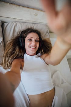 Woman taking pictures of herself in pajamas in bedroom on bed