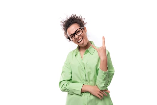 young european brunette curly woman dressed in light green shirt wears glasses for vision correction.