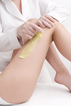 Closeup view of cosmetologist removing hair on women legs using hot wax. Quick sudden movement of cloth with green hot wax in professional beauty salon. Part of photo series.