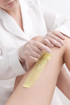 Closeup view of cosmetologist removing hair on women leg using hot wax. Quick sudden movement of cloth with green hot wax in professional beauty salon. Part of photo series.