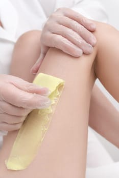 Closeup view of cosmetologist removing hair on female leg using hot wax in professional beauty salon. Depilation with hot wax in beauty salon. Part of photo series.