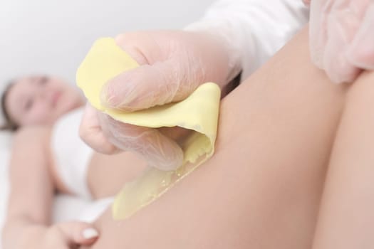 Waxing process - closeup view of quick sudden movement of cloth with green hot wax in professional beauty salon. Cosmetologist removing hair on women leg. Part of photo series.