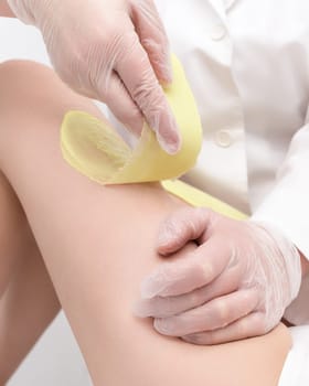 Closeup of beautician hands doing depilation to woman legs with green hot wax in beauty salon. Part of photo series.