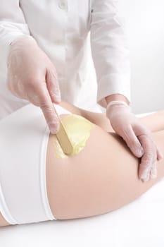 Beautician in gloves applying green hot wax on woman buttocks using spatula. Depilation process with hot wax in beauty salon. Part of photo series.