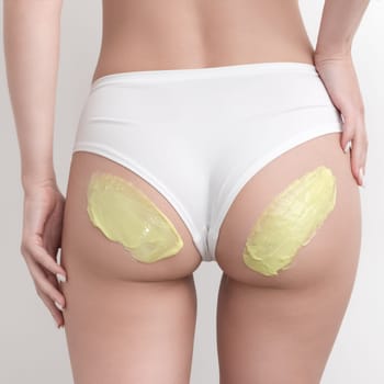 Green hot wax on woman buttocks. Healthy female slim body in white panties during hair removal procedure in professional beauty salon. Bikini hair removal epilation with wax. Part of photo series.