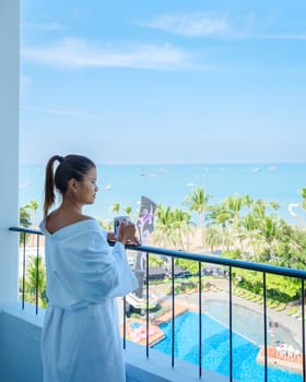 a Asian woman on vacation drinking coffee in the morning looking out the window over the beach and ocean during a luxury holiday