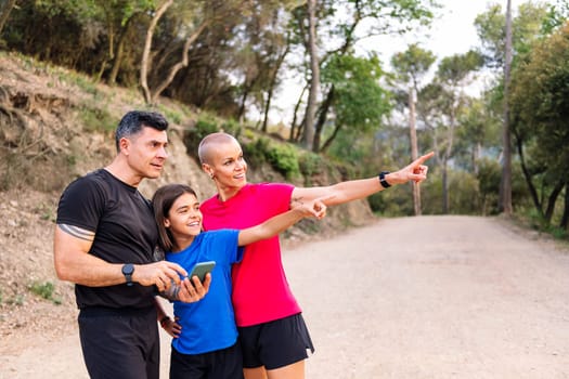 sporty family using a mobile phone to decide the route of their trail running training, concept of sport with kids in nature and active lifestyle