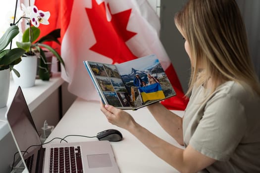 A female hand holds a small canada flag and a laptop on the background of the university. Close up. High quality photo