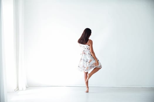 brunette woman in a floral dress stands with her back in a bright room