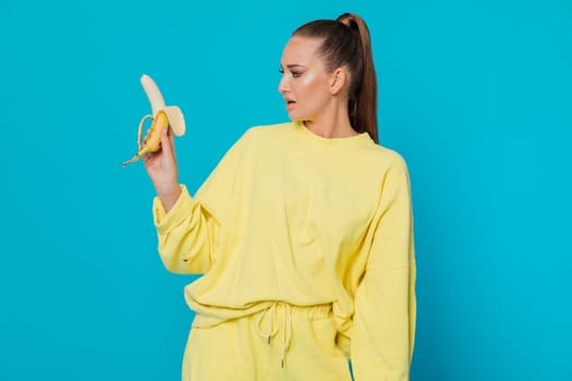 woman in yellow clothes stands with a banana and looks at it