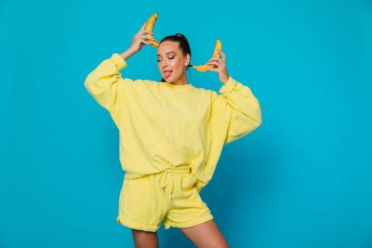 a woman in yellow clothes stands on a blue background with bananas at her head