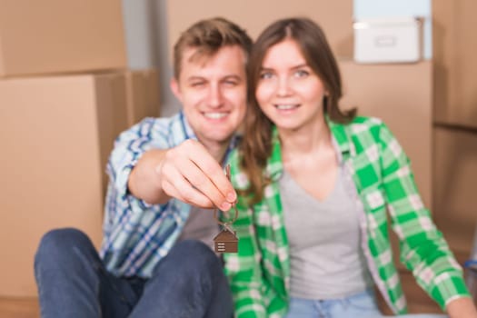 Happy young couple sitting on floor near boxes. Young family moving to new home. Woman and man showing keys and smiling at camera.