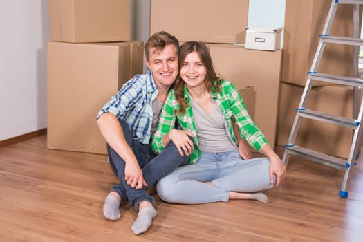 Moving to a new house and repairs in the apartment. Love couple sitting in an empty apartment among boxes.