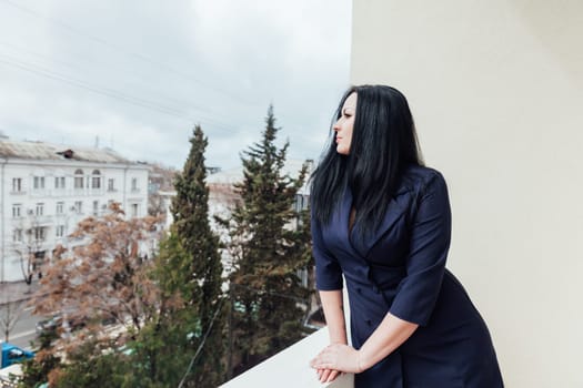 fashionable woman in a black dress stands on a bright balcony