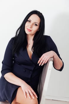 business woman in a black dress sits on a chair on a white background