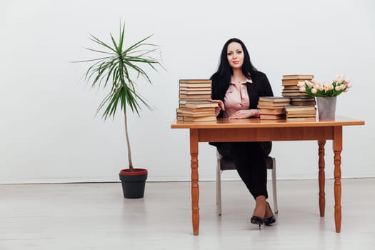 a woman sitting at a table with a stack of books many books cabinet library