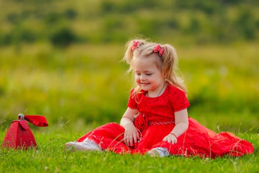 little girl in a red dress sits on a green lawn