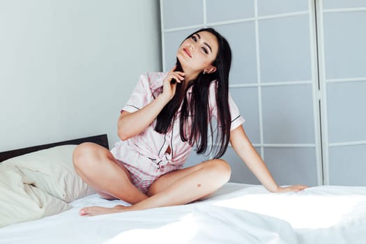 woman in pajamas sitting on a bed in the morning in the bedroom woke up