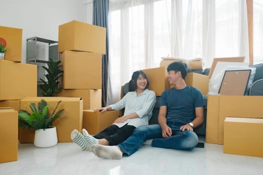 Happy couple sitting and rest with cardboard boxes in new house at moving day. New house owner and real estate concept.