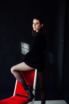 brunette woman in black clothes sitting on a chair in a dark room