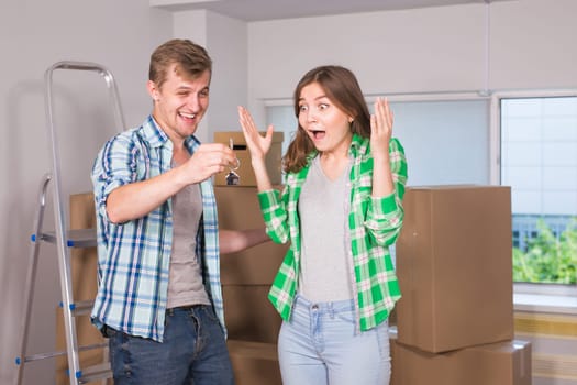 home, people, moving and real estate concept - Surprised woman looking at house keys in the hand of a man.