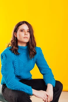 woman in a warm sweater in winter clothes sits at a yellow background