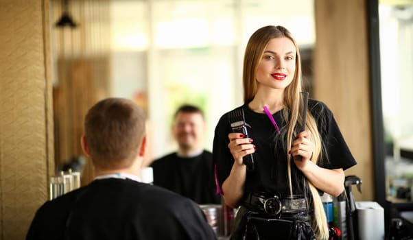 Hairstylist Hold Razor and Comb for Male Haircut. Female Hairdresser Showing Electric Shaver and Hairbrush for Styling Man Hairdo. Shave Client in Barbershop. Stylist with Tool Looking at Camera Shot