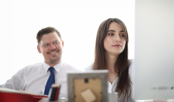 Portrait of designers sitting in modern workplace and looking at something. Gorgeous woman in trendy white blouse discussing art project with colleague. Blurred background