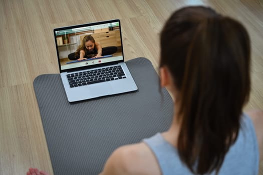 Calm woman doing yoga watching tutorial lesson on laptop in living room.