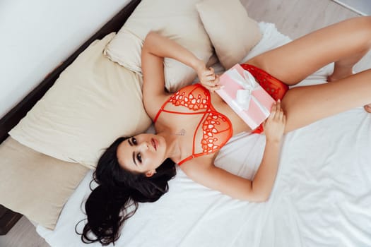 woman in underwear lies on the bed in the bedroom with a gift