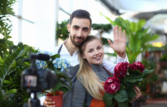 Happy Vlogger Holding Domestic Flowers in Pot. Man and Woman Florist Recording Video for Plant Vlog. People Showing Blue and Red Hydrangea in Flowerpot to Camera. Gardener Looking at Camera Shot