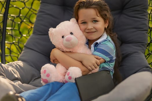 child hugging a teddy bear while sitting in a hanging chair